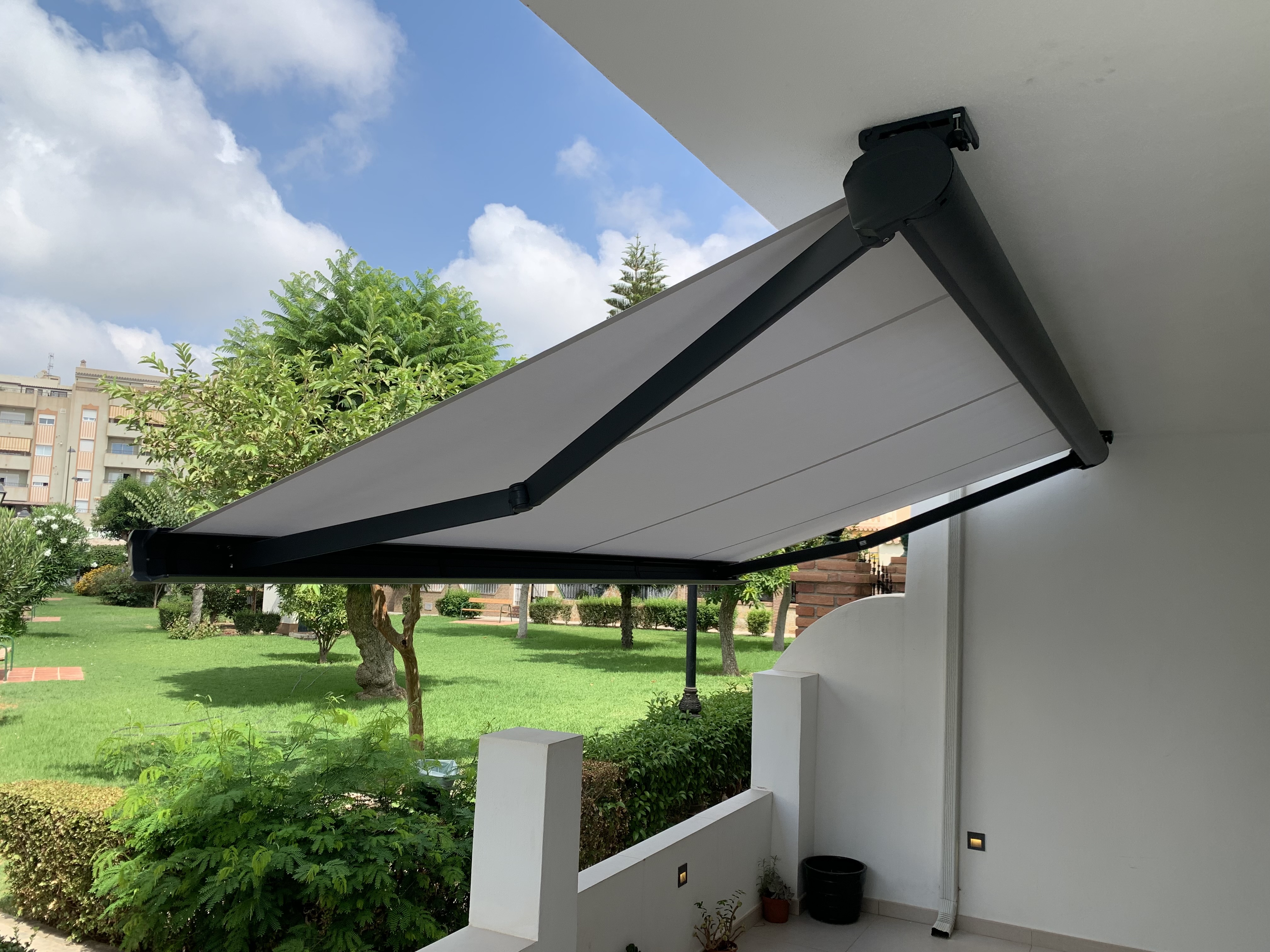 Toldo retráctil gris extendido desde balcón con vistas al jardín - Servitoldos Daniel